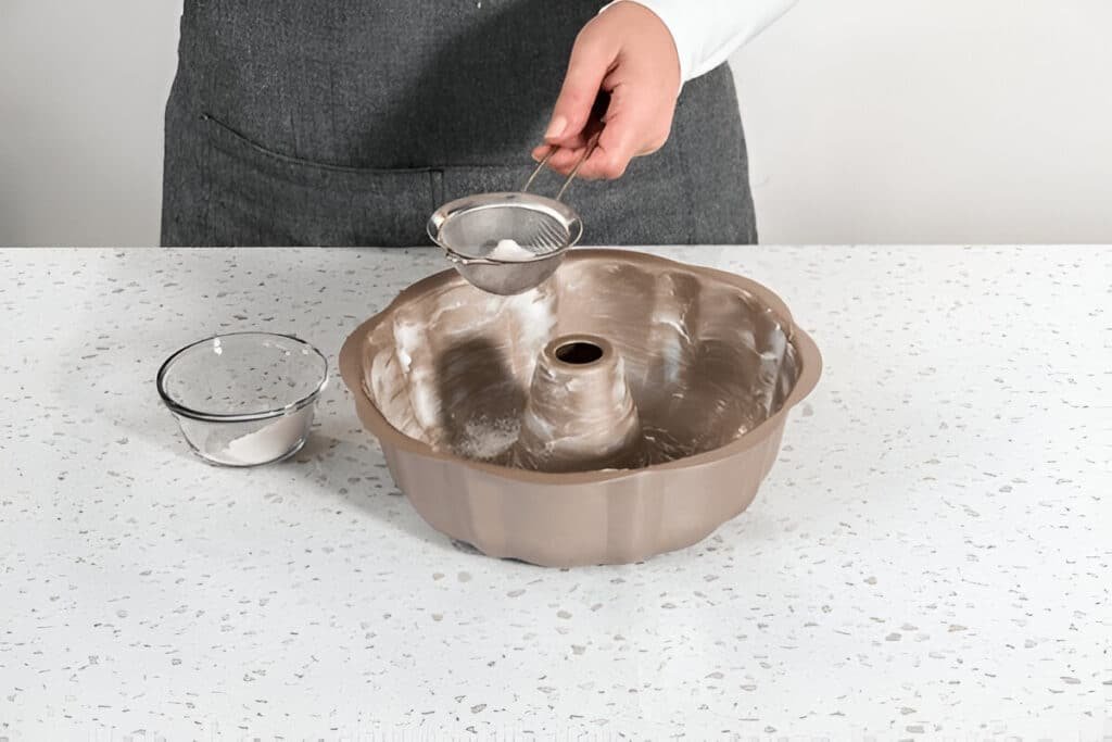 : Dusting flour into a greased bundt pan before baking