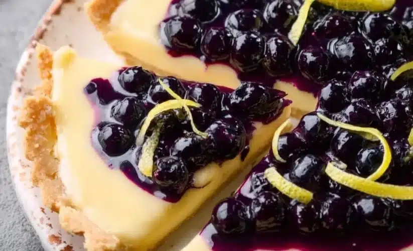 Creamy lemon tart topped with vibrant blueberry sauce on a white plate.